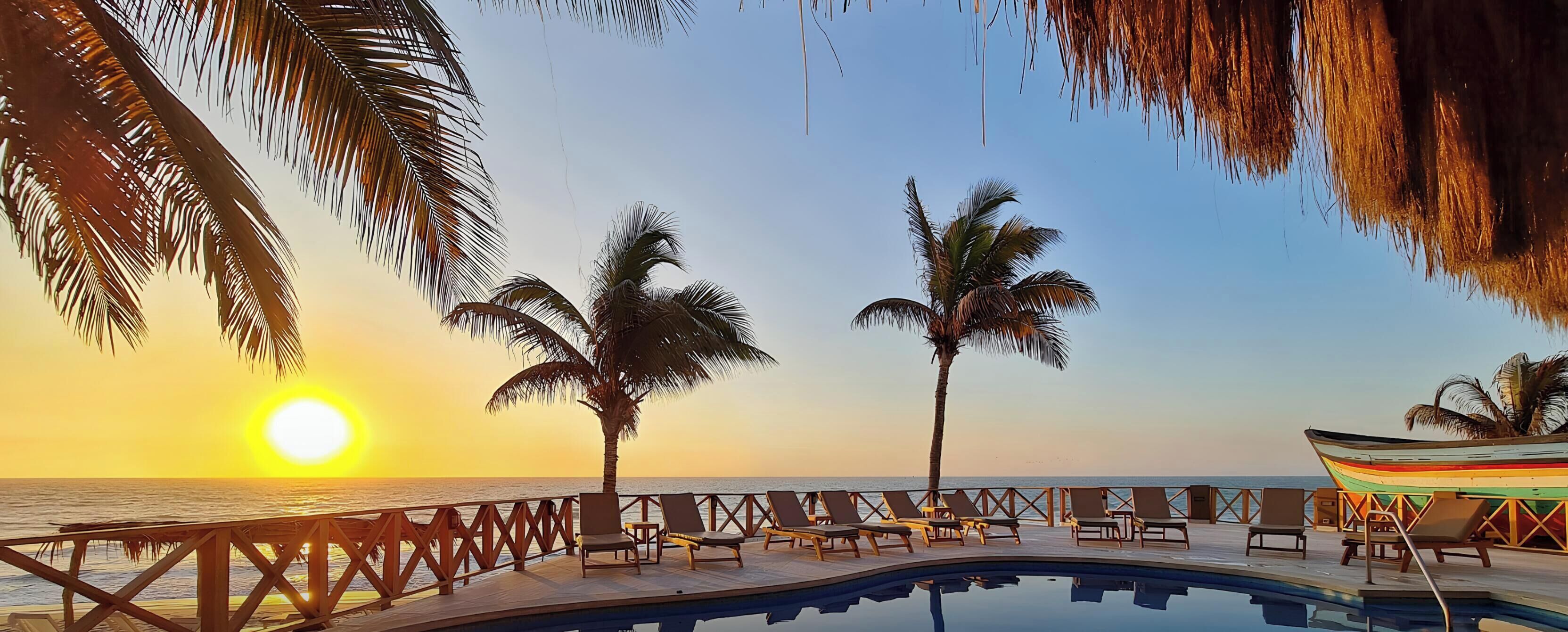 Un espace aménagé au bord de la piscine, avec des chaises longues et un bateau, offrant une vue sur l’océan au coucher du soleil.