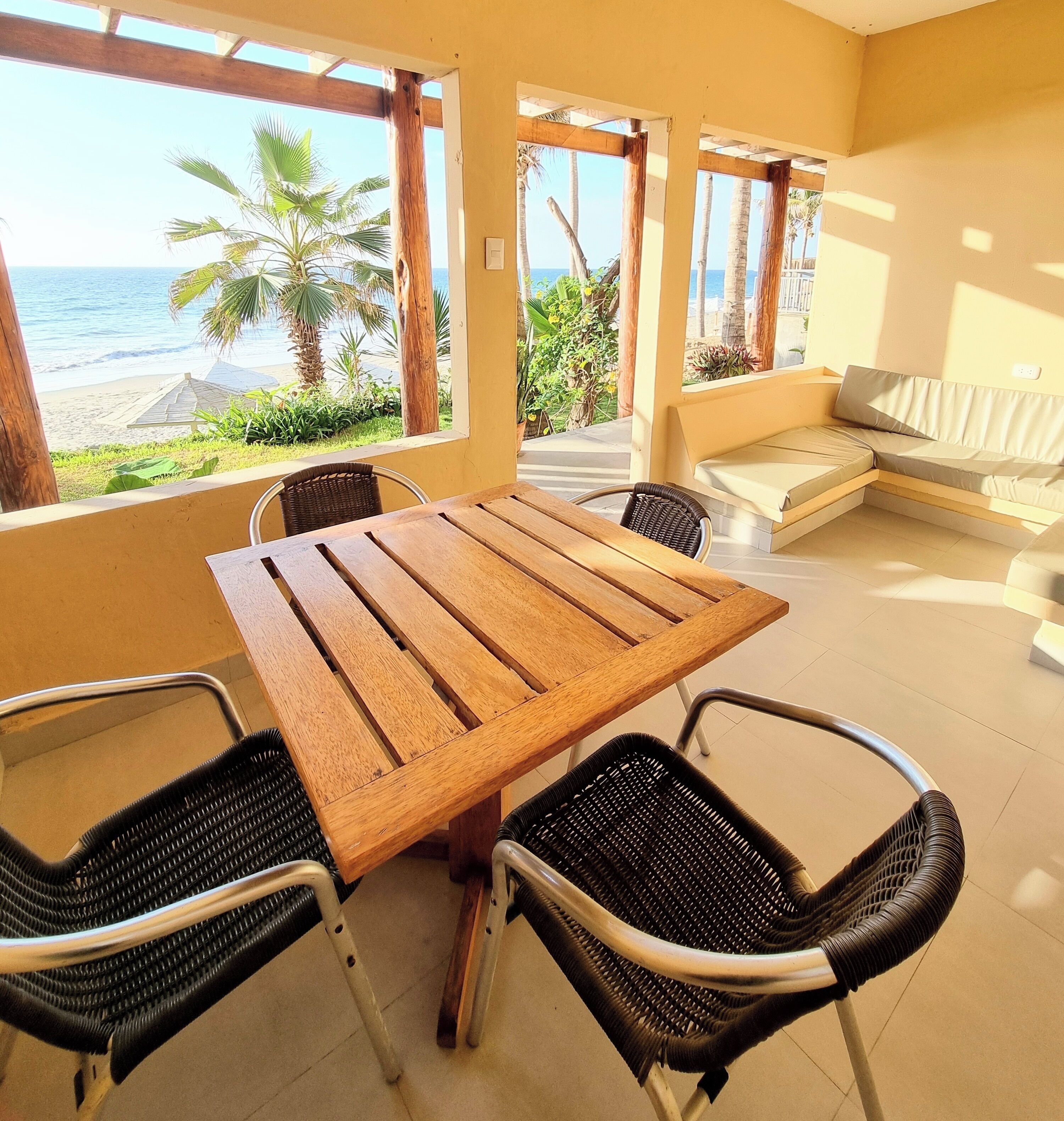 Una habitación con una mesa de madera y cuatro sillas, un sofá y vista a la playa.