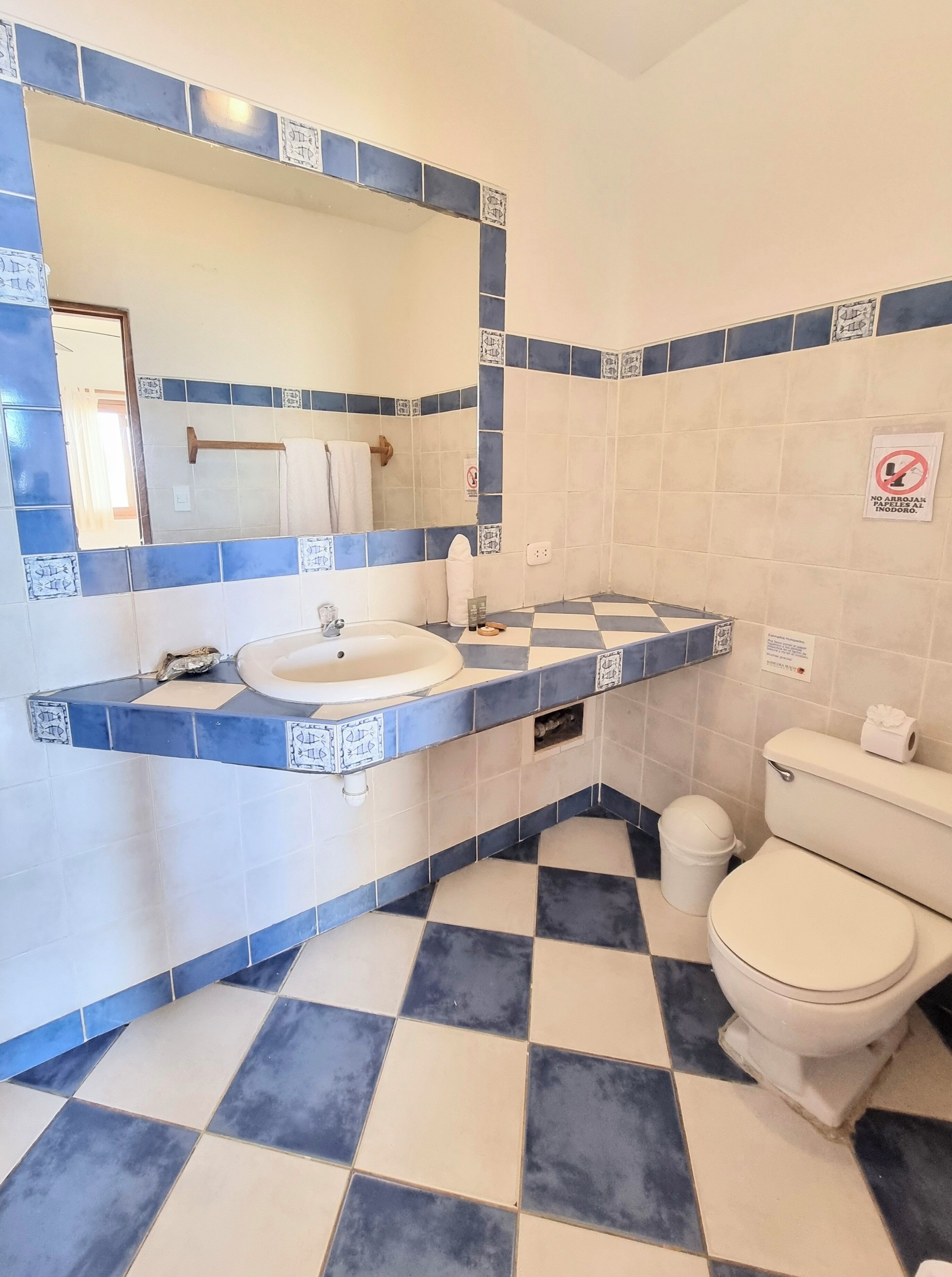 A bathroom with a sink, mirror, toilet, and checkered floor tiles.