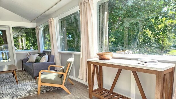 Een moderne woonkamer met een bank, een houten stoel, een salontafel en een groot raam met gordijnen.