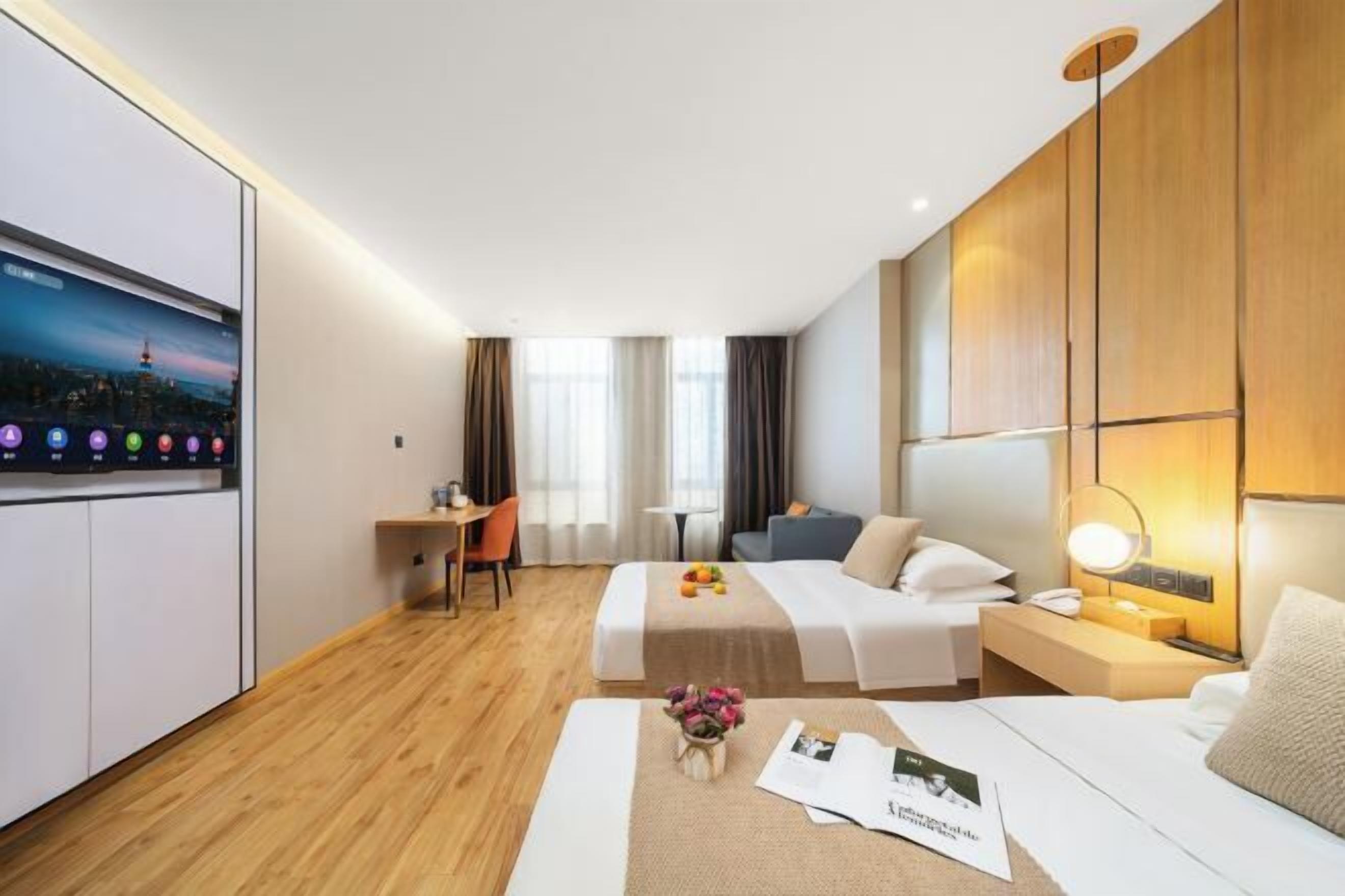 Una habitación de hotel con cama, mesita de noche, lámpara, escritorio, silla y televisor en la pared.