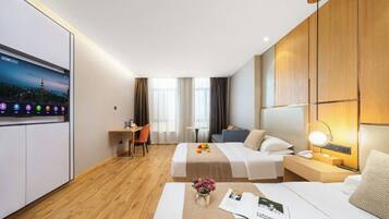 Una habitación de hotel con cama, mesita de noche, lámpara, escritorio, silla y televisor en la pared.