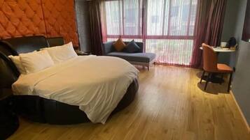 Quarto de hotel com uma cama grande, um sofá, uma mesa e vista para o exterior através de grandes janelas.