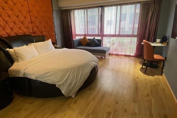 Une chambre d’hôtel dotée d’un grand lit, d’un canapé, d’un bureau et offrant une vue sur l’extérieur grâce à de grandes fenêtres.