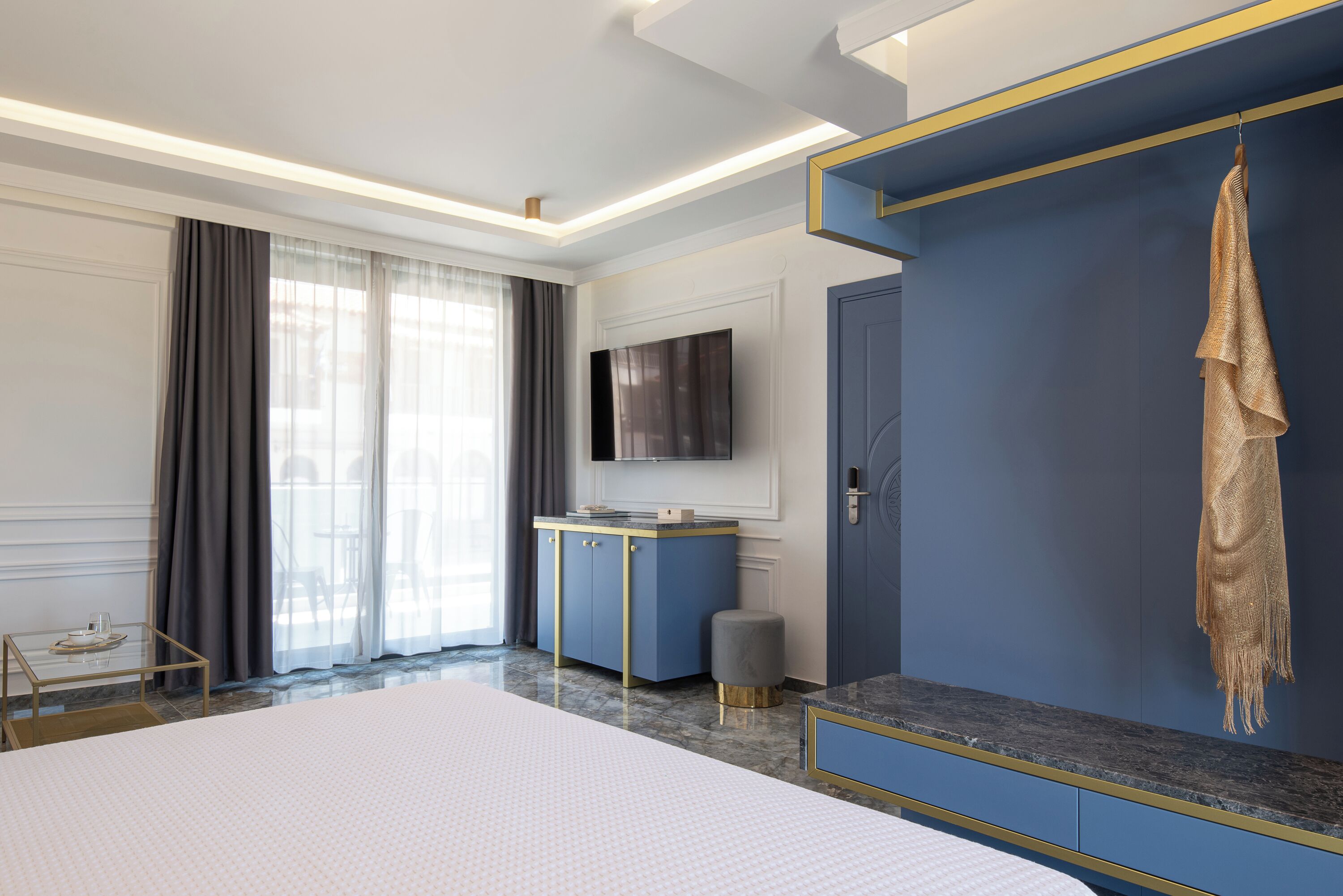 Ein modernes Hotelzimmer mit einem großen Bett, einem an der Wand befestigten Fernseher, einem Kleiderschrank und einem kleinen Tischchen mit Tablett.