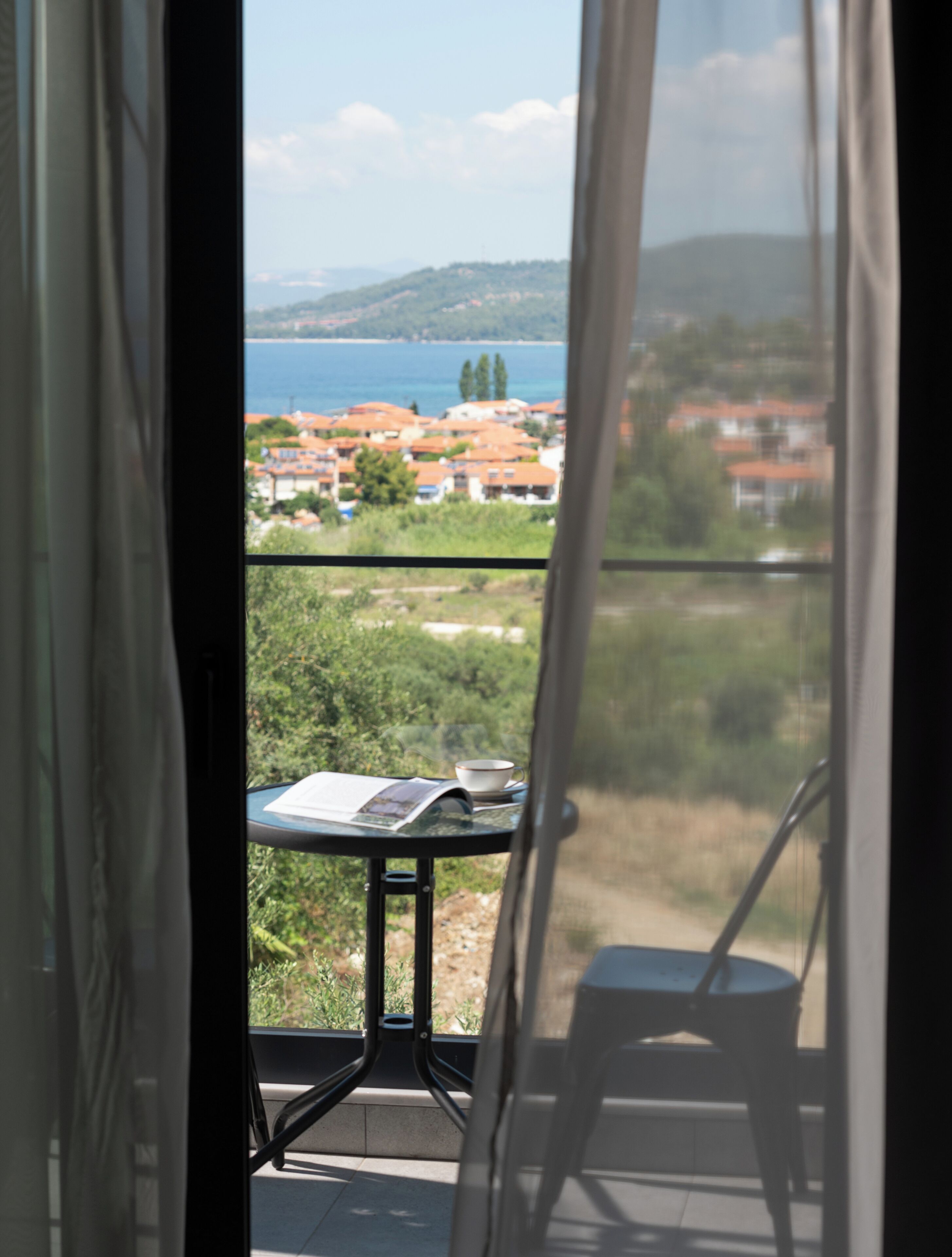 Ein Balkon mit Tisch und Stuhl, mit Blick auf eine Küstenstadt mit Häusern und einem Gewässer.