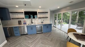 A modern kitchen with blue cabinets, a stainless steel refrigerator, and a large window overlooking a patio.