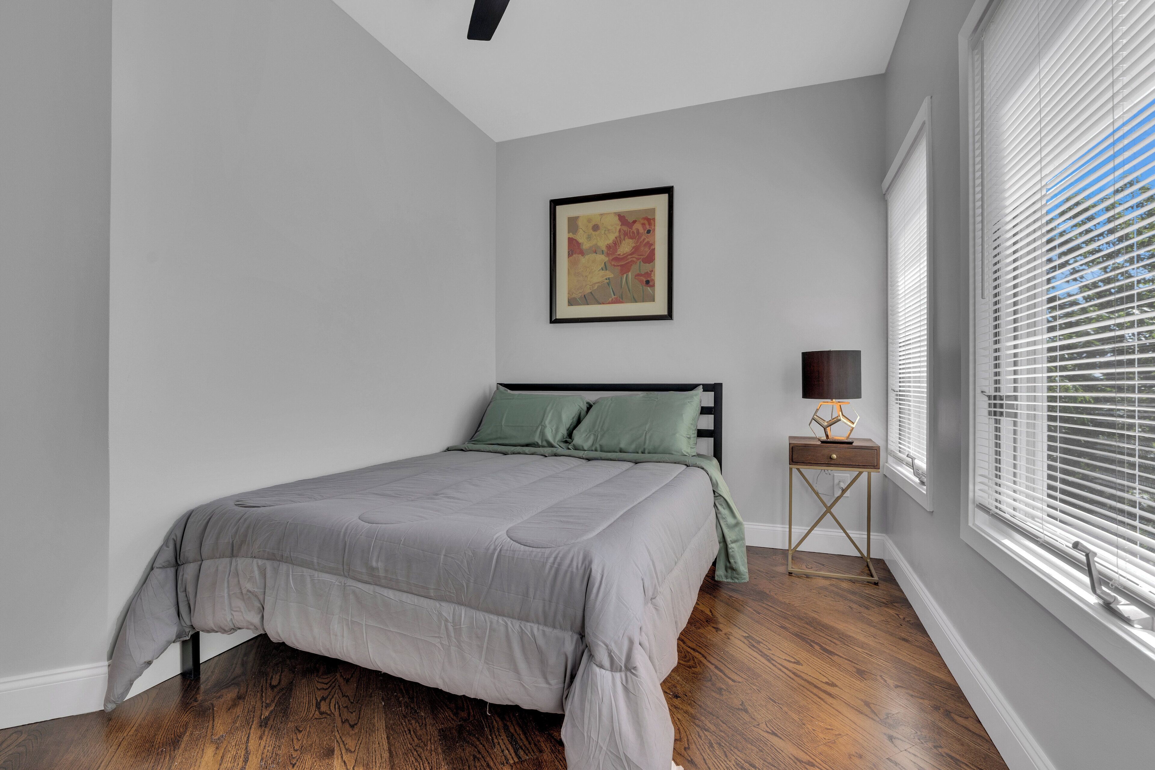 Une chambre à coucher avec un lit, une table de chevet, une lampe et une fenêtre avec des stores.