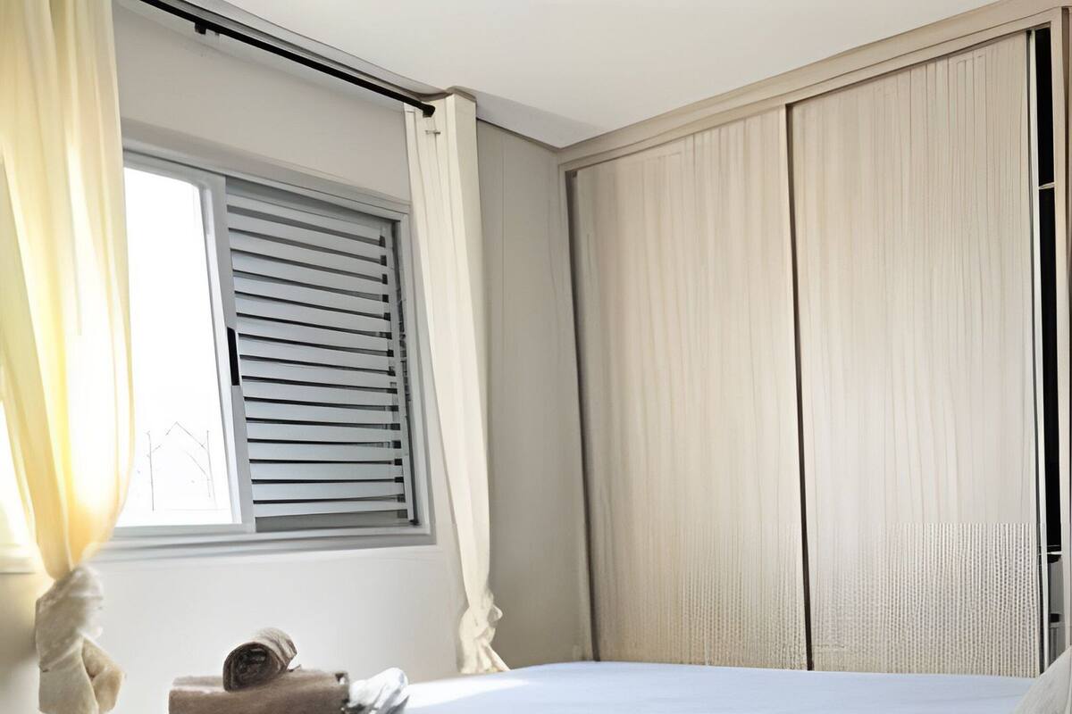 A bedroom with a bed, curtains, a window, and a wardrobe.