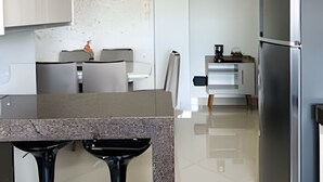 Une cuisine moderne dotée d’un plan de travail en granit, d’appareils électroménagers en acier inoxydable et d’un coin repas avec une table et des chaises blanches.