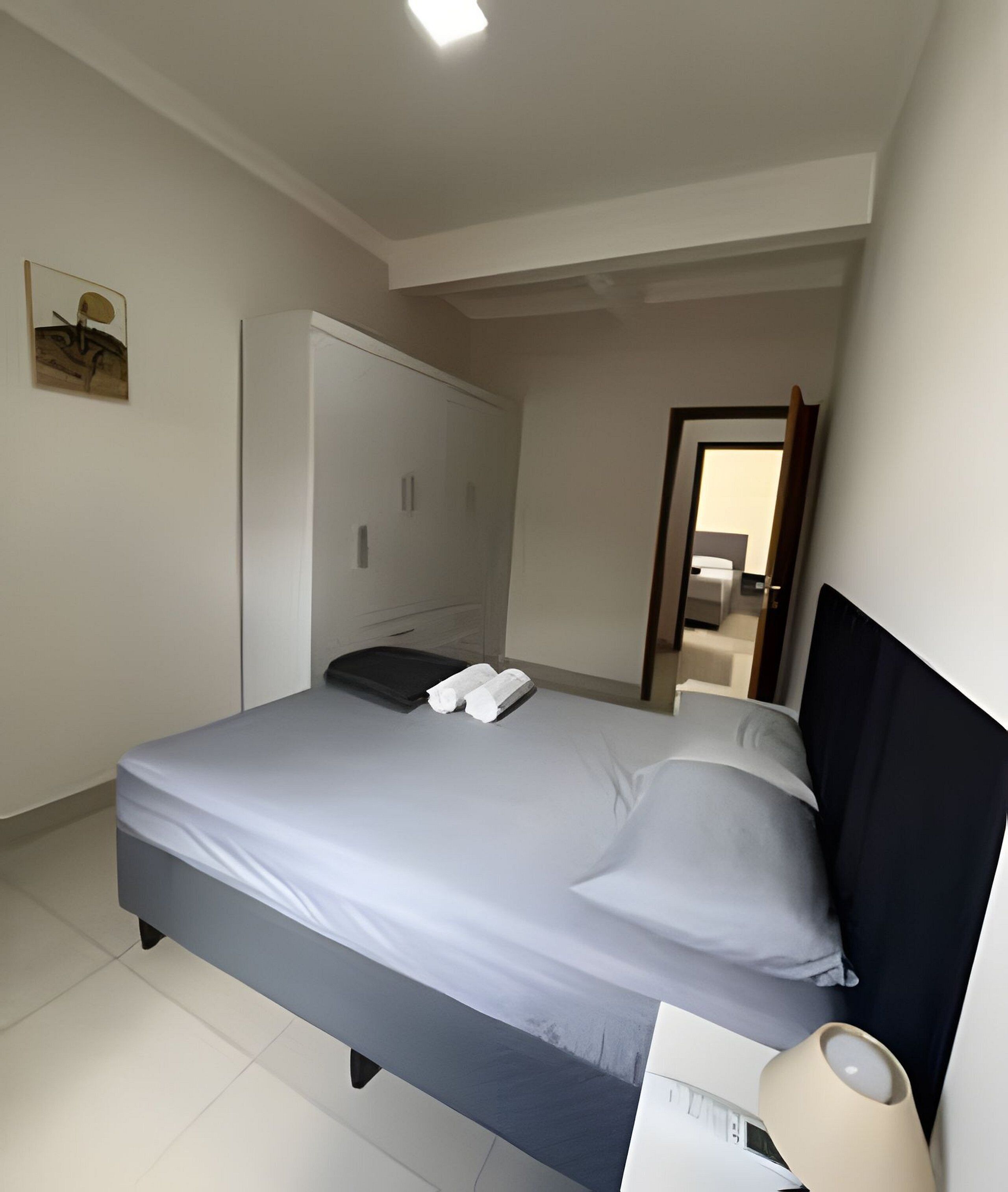 Un dormitorio con cama, armario, mesita de noche y lámpara.