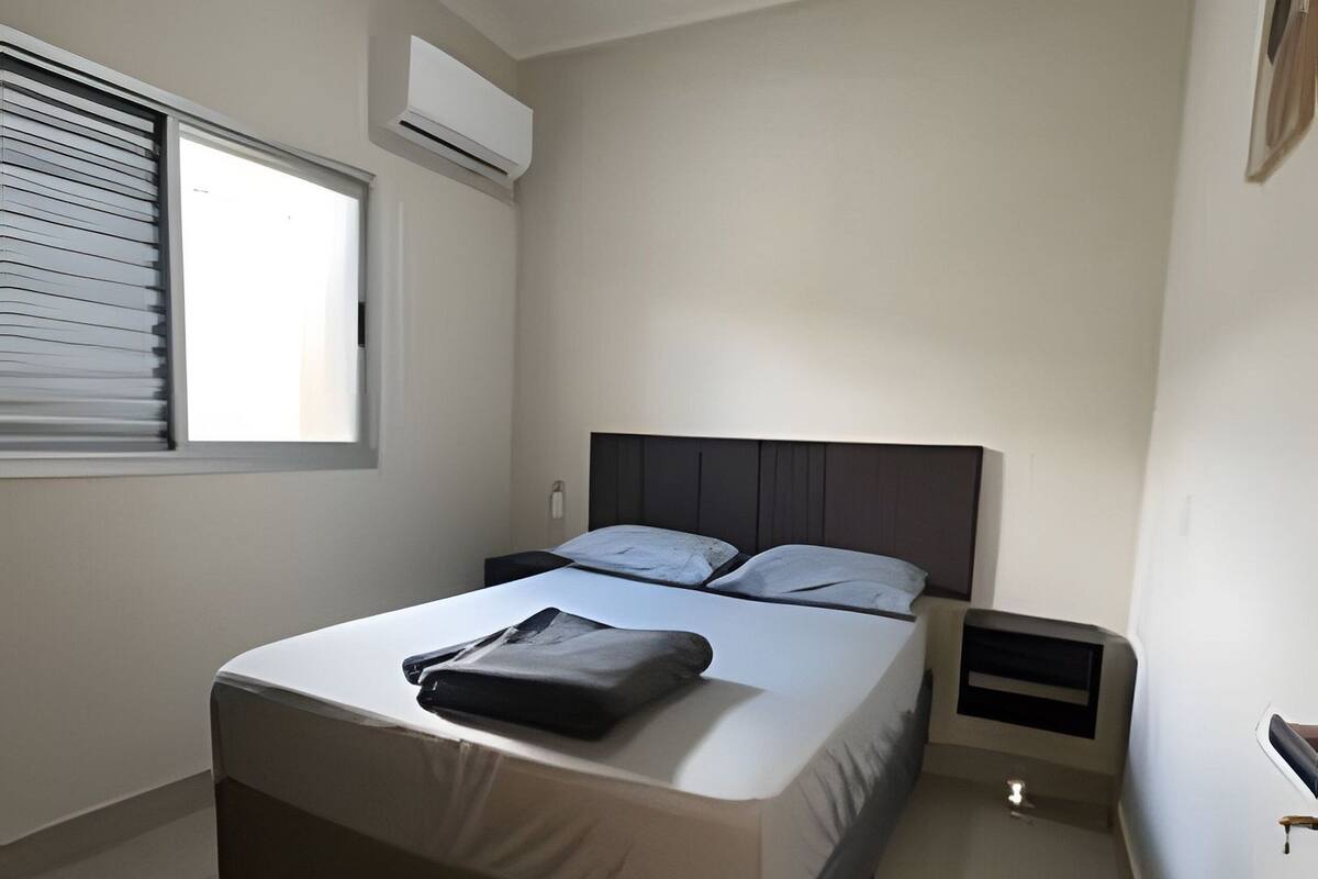 A modern bedroom with a large bed, a bedside table, a nightstand, and a window with blinds.