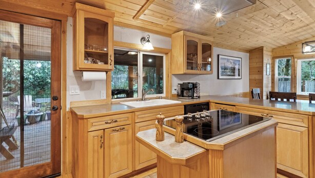 Una cocina de madera con una isla grande, alacenas empotradas y un ventanal con vista a un jardín.