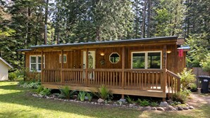 Una cabaña de madera con terraza, rodeada de un jardín y árboles.