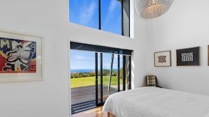 Een slaapkamer met een groot bed, uitzicht door een schuifdeur op een terras, en kunstwerken aan de wanden.
