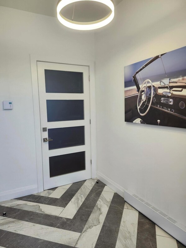 A hallway with a white door, a ceiling light, and a framed picture of a car interior on the wall. - South Beach Residences (St. John's)