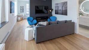 Una sala de estar moderna con un sofá gris, sillones azules, un televisor de pantalla plana y una chimenea.