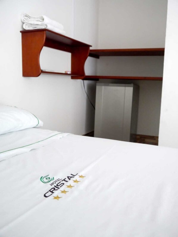 A hotel room with a bed, a wooden shelf above it, and a wall-mounted radiator. - Hotel El Cristal (Muzo)