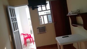 Une petite chambre d’hôtel comprenant un lit, un bureau, un téléviseur fixé au mur, une fenêtre et une porte donnant sur un balcon.
