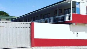 Un bâtiment à la façade blanche et rouge, doté d’une entrée fermée par un portail et d’un balcon avec des balustrades.