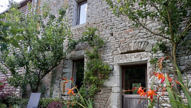A stone building with a wooden door and windows, surrounded by greenery and a chair. - BRETON MANOR (Theix-Noyalo)
