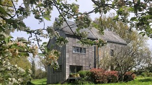 A house with a sloped roof, surrounded by a well-maintained lawn and flowering trees. - BRETON MANOR (Theix-Noyalo)