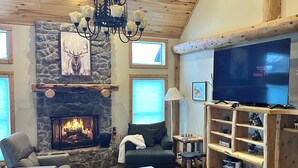 Ein gemütliches Wohnzimmer mit Kamin aus Stein, einem großen Fernseher und einer Holzunterhaltungseinrichtung.