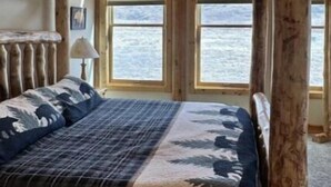 Ein rustikales Cabin-Zimmer mit Bett, Holzbalken und großen Fenstern mit Blick auf ein Gewässer.