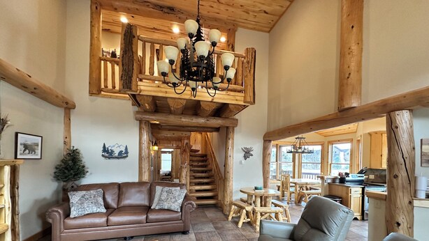 Ein geräumiger Wohnbereich mit braunem Ledersofa, einem Holztisch und einem Essbereich mit hölzernen Bänken und einer Kronleuchter.