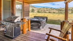 Eine Holzterrasse mit Grill, Whirlpool und Sitzbereich mit Blick auf eine grüne Landschaft.
