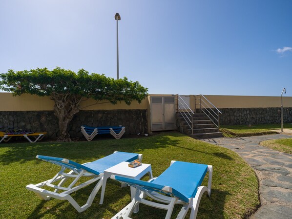 Un patio con dos sillones azules, una mesa pequeña, un árbol y una escalera que lleva a un nivel superior.
