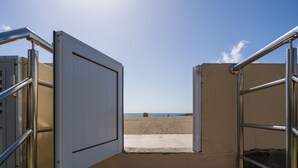 Acceso a la playa con barandillas metálicas y un camino de hormigón que lleva a la arena.