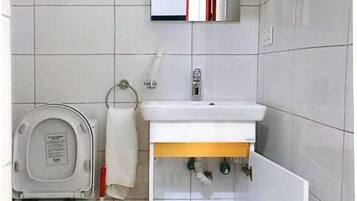 A bathroom with a toilet, sink, mirror, and storage cabinet.