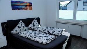 A modern bedroom with a black sofa bed, floral-patterned bedding, a nightstand, and a window with blinds.