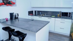 A modern kitchen with white cabinets, a grey countertop, a sink, a microwave, and two black bar stools.