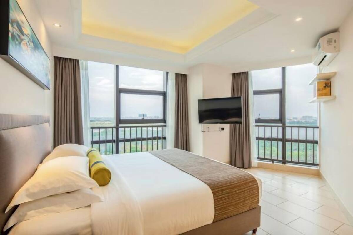 A hotel room with a bed, a TV, and large windows offering a city view.