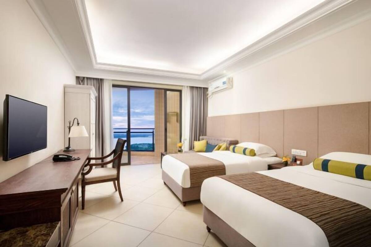 A hotel room with two beds, a desk, a TV, and a view of the ocean.