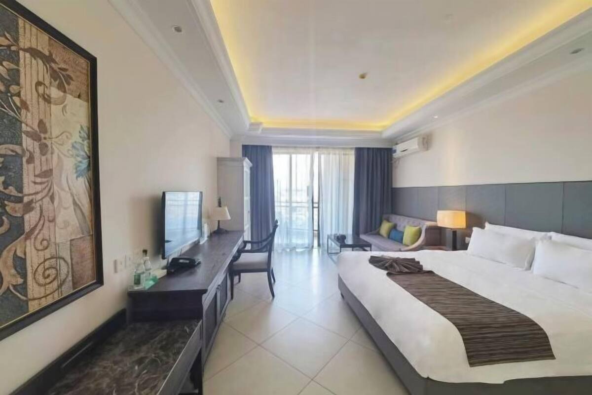 A hotel room with a bed, desk, chair, and a large painting on the wall.