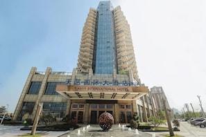A modern hotel with a prominent glass facade, a large entrance with a sign, and a decorative spherical sculpture in front. - Tianyi International Hotel (Nandujiang Meilan Airport Branch) (Haikou)
