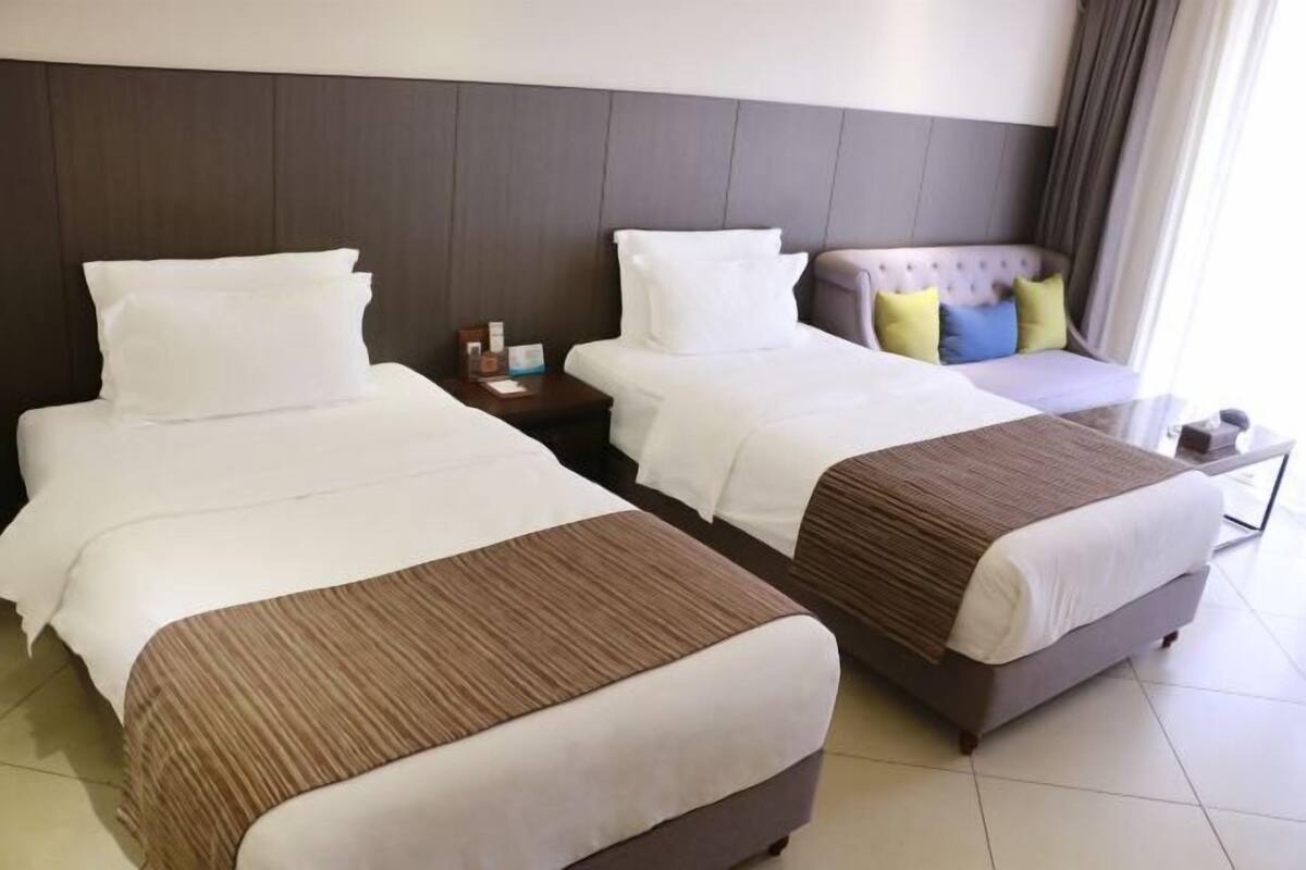 A hotel room with two beds, a nightstand, and a seating area with cushions.