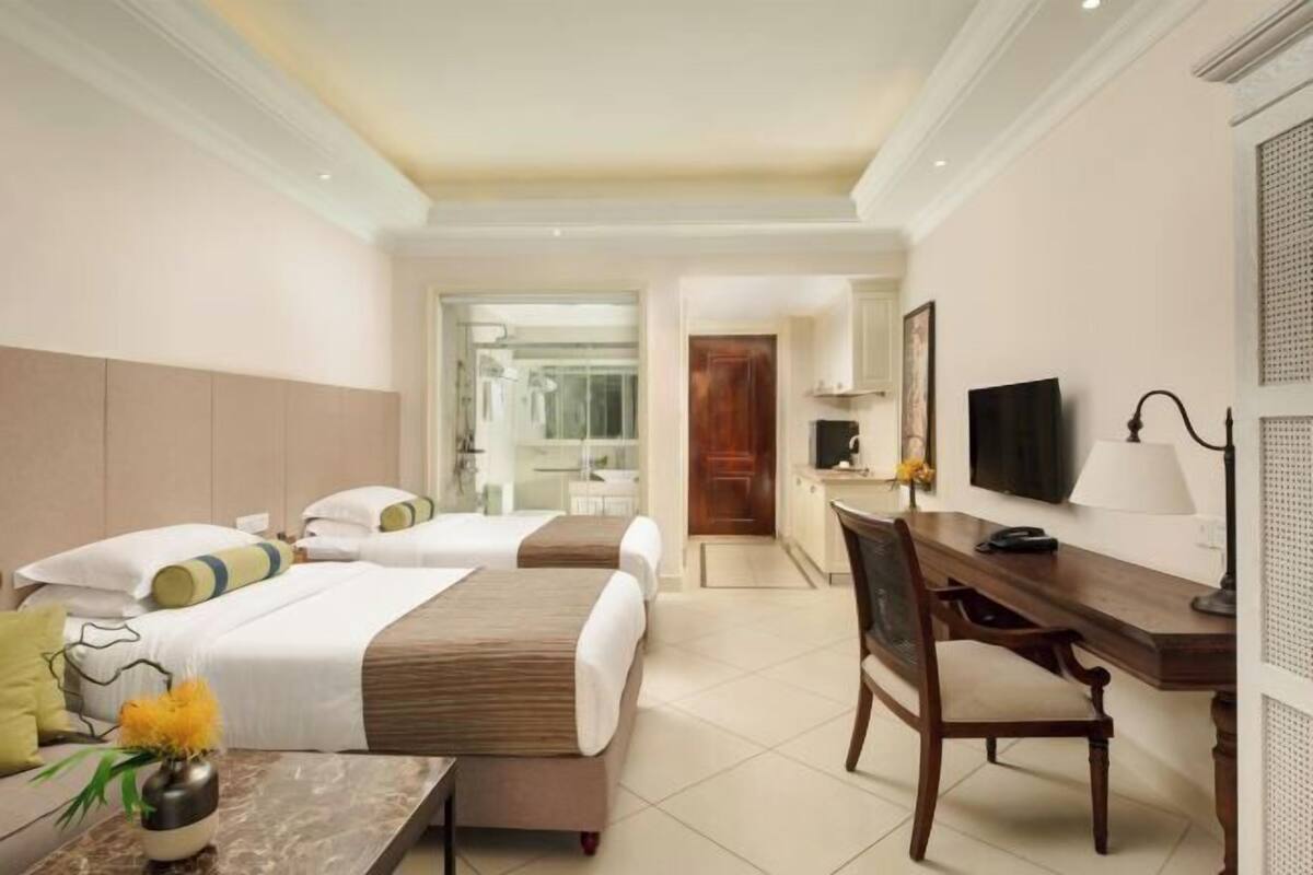 A hotel room with two beds, a desk, a chair, a TV, and a bathroom visible through an open door.
