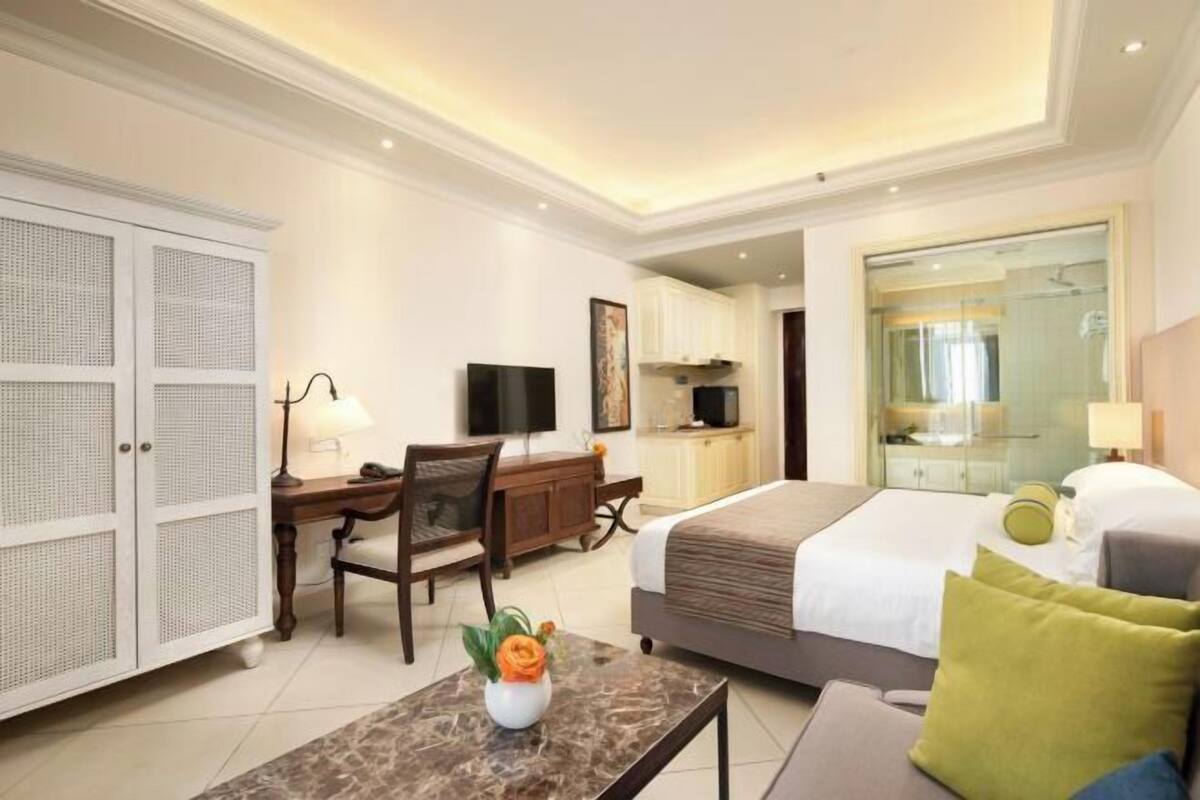 A hotel room with a bed, desk, chair, TV, wardrobe, and a bathroom with a mirror.