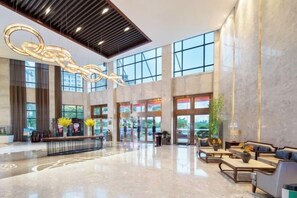 A spacious lobby with a high ceiling, large windows, and a reception desk. - Tianyi International Hotel (Nandujiang Meilan Airport Branch) (Haikou)
