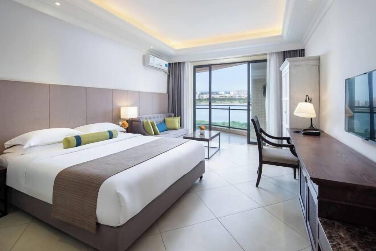 A hotel room with a bed, a desk, a chair, a TV, and a large window with a view.