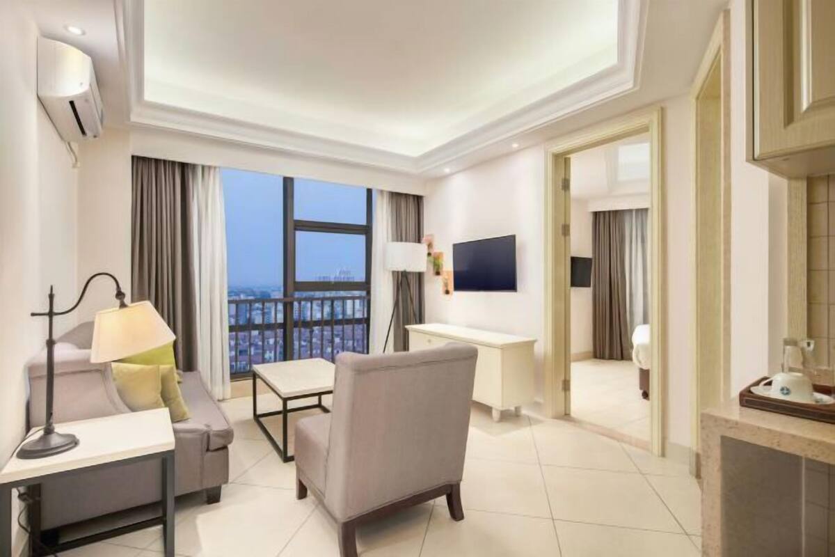 A hotel room with a balcony, a desk, a chair, a sofa, and a TV.