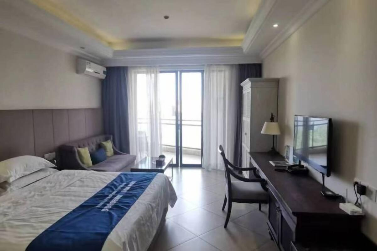A hotel room with a bed, a desk, a chair, a television, and a large window.
