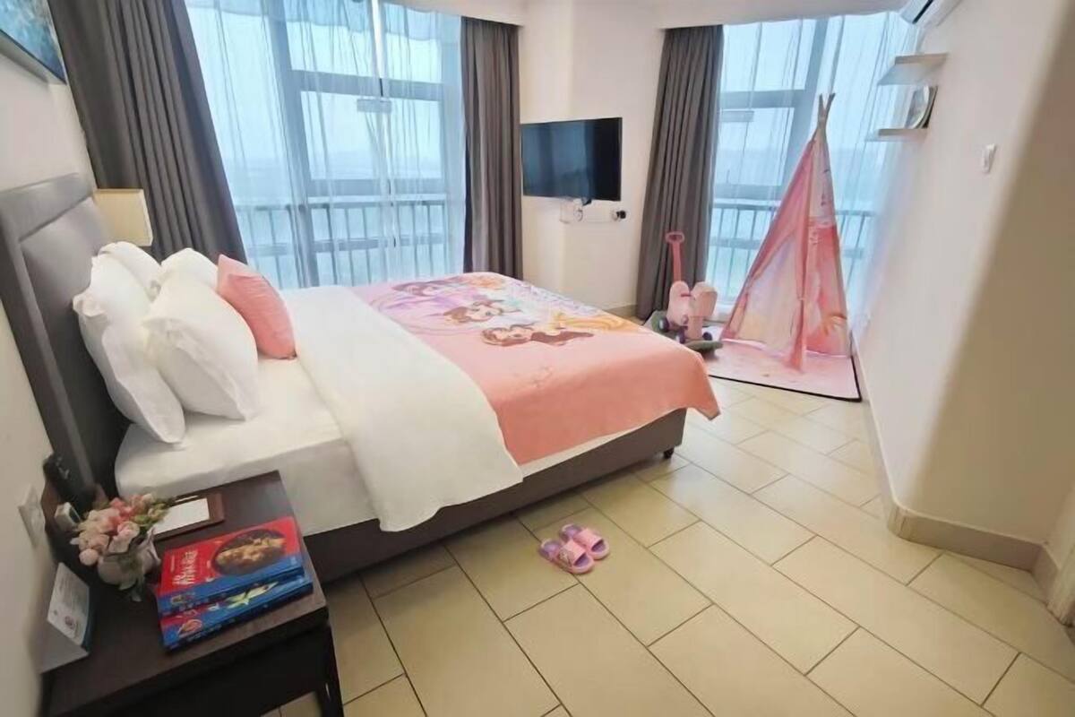A hotel room with a bed, a TV, a balcony with a view, and a small table with items on it.