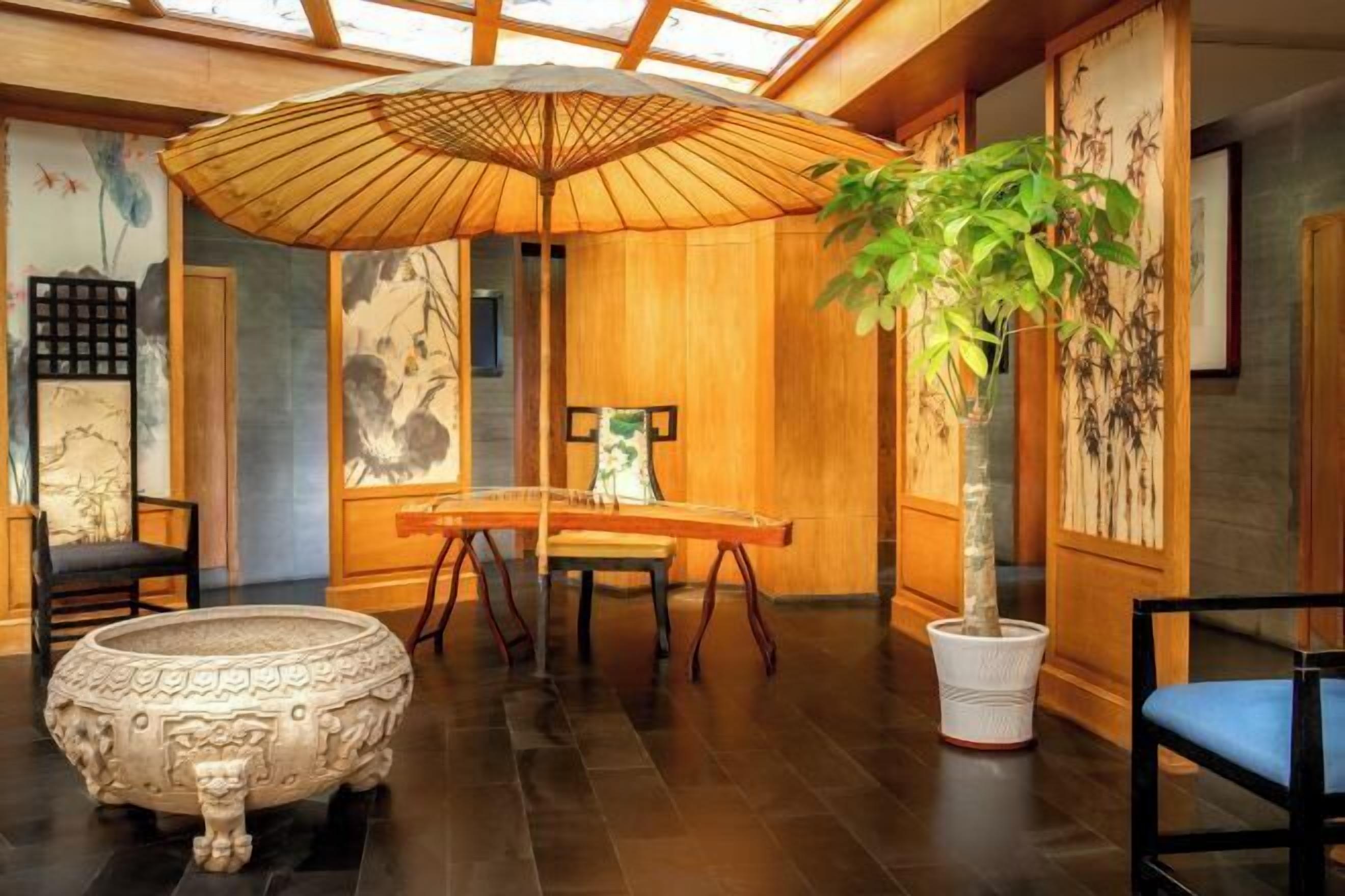 A traditional Japanese room with tatami flooring, a shoji screen, a wooden table, a hanging scroll, and a bonsai tree.