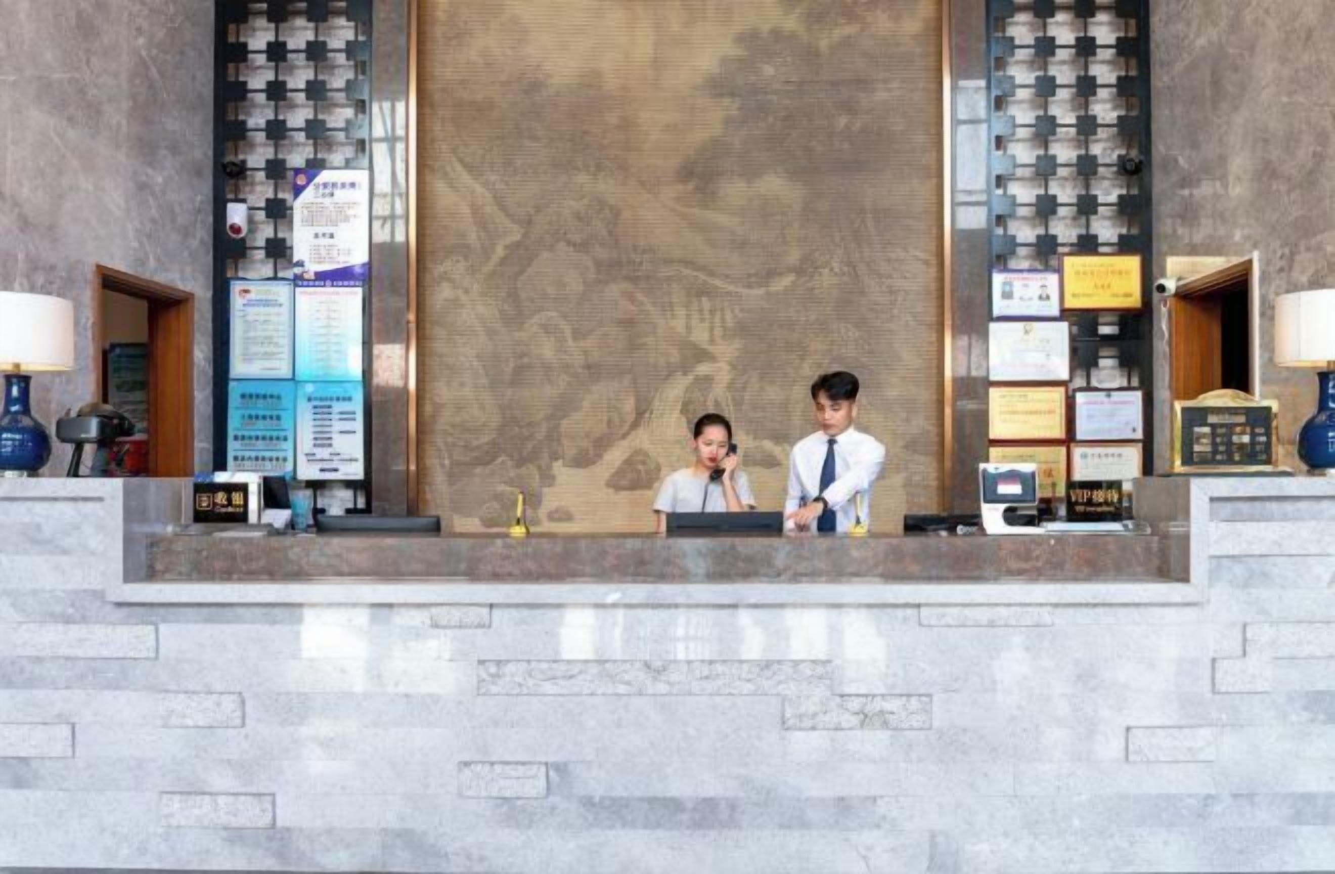 A reception desk with two staff members, a large wall mural, and various informational signs.