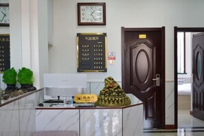 Un espace d’accueil doté d’un comptoir en marbre, de plusieurs horloges, d’un tableau d’affichage et d’une porte de style traditionnel.